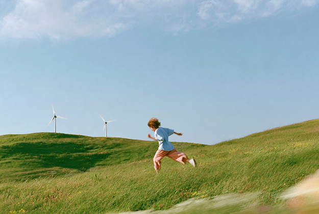 A child running down a grassy hill past wind turbines
