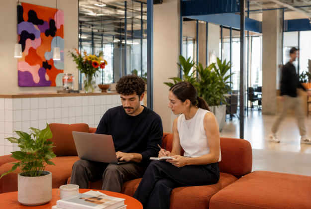 Two colleagues working on laptops in an office lounge